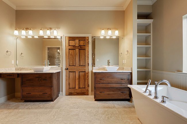 Dual vanities with custom sinks in a private large master bath. Custom vessels sinks on top of solid countertops with solid wood drawers for storage. Separate large mirrors with custom lighting above each vanity. Built in wooden shelves from floor to ceiling also allow storage.