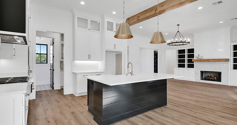 This kitchen features a nice kitchen island with custom lighting. The kitchen also has hardwood floors.
