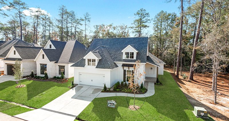 The image features an aerial view of a newly constructed two-story house with a steep gable roof, white exterior walls, and a two-car garage.