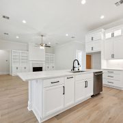 A modern kitchen opens into the living room, featuring a large island with a sink, white cabinetry, and black hardware.