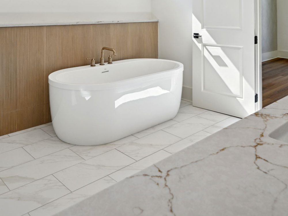 17-5040 Twin River Soaking Tub This serene bathroom moment captures a freestanding soaking tub that exudes modern simplicity and comfort. The tub’s clean, curved silhouette sits against a textured wood-paneled wall detail, adding warmth and organic contrast to the cool white finishes.