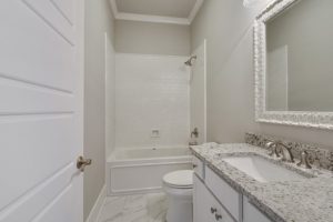 Bright secondary bathroom with crown molding and oversized vanity. This bathroom has a shower tub combo that is surrounded by custom white tile.