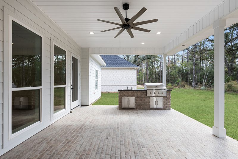 21-5048 Twin River Place Brick Porch Floor The patio opens up to a backyard bordered by natural greenery, enhancing the outdoor living experience.