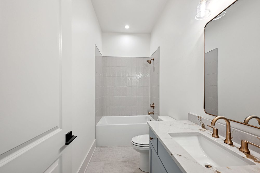 23-5040 Twin River Secondary Bath A minimalist arched mirror and clear globe sconce complete the polished look, while recessed lighting ensures the room feels bright and airy.