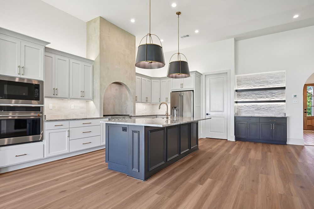 7-5040 Twin River Kitchen Overview The tall arched range hood and oversized pendant lights add architectural interest and elegance, while a built-in wet bar with floating stone shelves offers extra style and storage.
