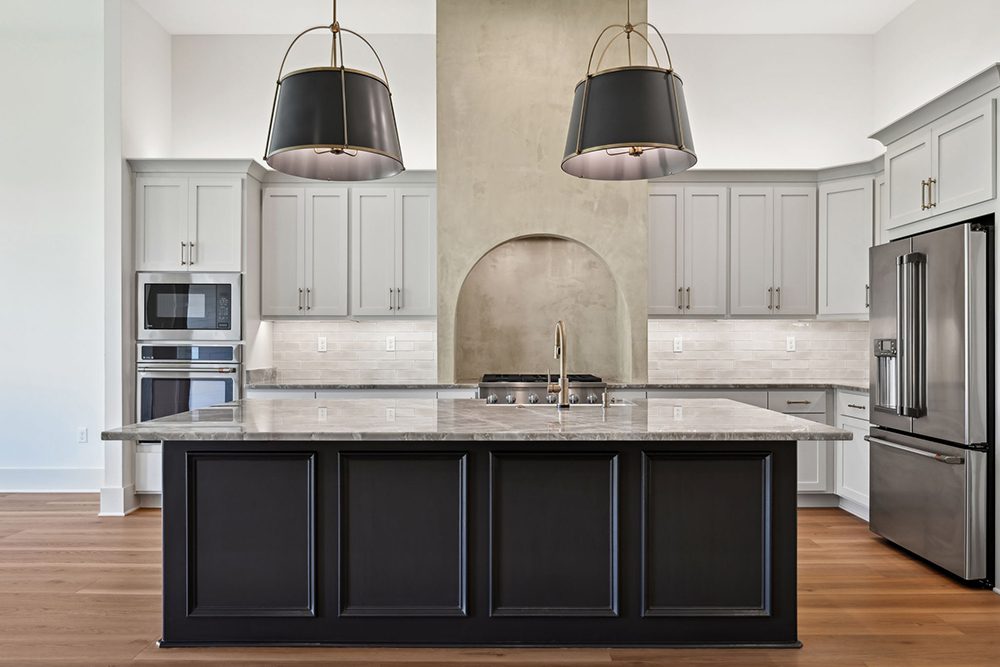 8-5040 Twin River Custom Kitchen Island A unique arched niche behind the cooktop draws the eye, flanked by a stylish plaster-style range wall that adds texture and character. The soft taupe subway tile backsplash and under-cabinet lighting create a cohesive and inviting atmosphere, while wide-plank wood flooring grounds the entire space with warmth. This kitchen is not only functional but also a designer showcase—perfect for entertaining or everyday culinary inspiration.