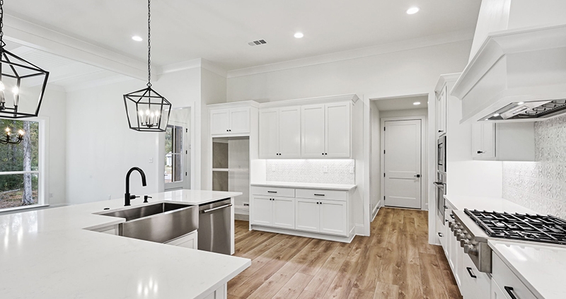 The image shows a modern kitchen with white cabinetry, a large central island with an undermount sink, and contrasting black fixtures.